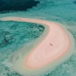 Couple standing on Taka Makassar's crescent-shaped reef from above.
