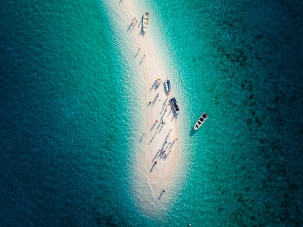 Aerial shot of Taka Makassar sand dune surrounded by turquoise water with boats and visitors